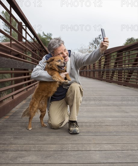 Caucasian man taking photograph with dog on bridge