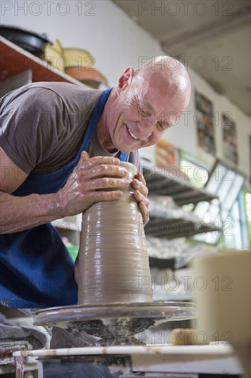 Older Caucasian man forming pottery on wheel in ceramics studio