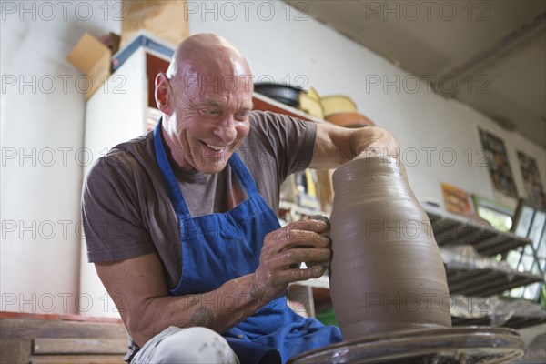 Older Caucasian man forming pottery on wheel in ceramics studio