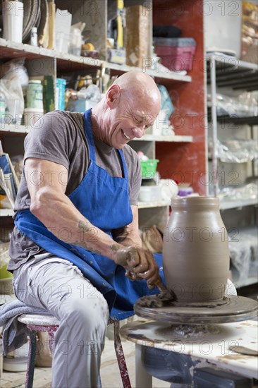 Older Caucasian man forming pottery on wheel in ceramics studio