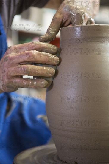 Older Caucasian man forming pottery on wheel in ceramics studio