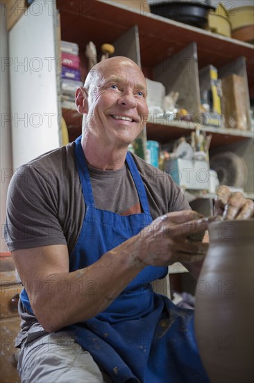 Older Caucasian man forming pottery on wheel in ceramics studio