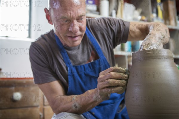 Older Caucasian man forming pottery on wheel in ceramics studio