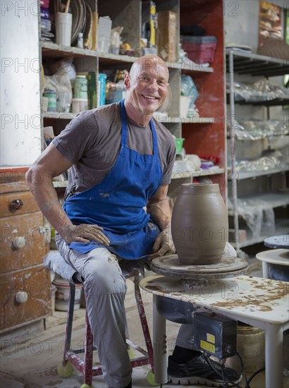 Older Caucasian man forming pottery on wheel in ceramics studio