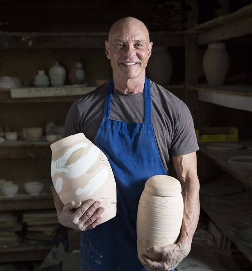 Proud older Caucasian man holding pottery in ceramics studio