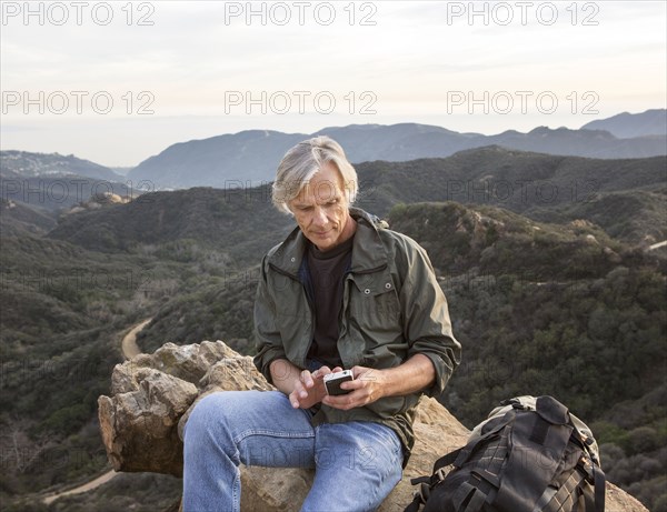 Older Caucasian man using cell phone on rocky hilltop