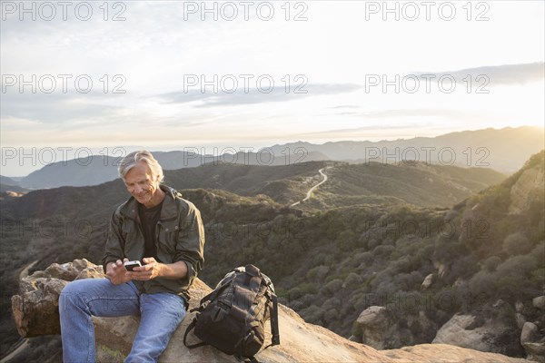 Older Caucasian man using cell phone on rocky hilltop