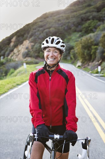 Caucasian woman with bicycle smiling on remote mountain road