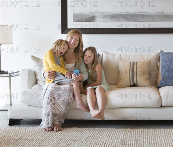 Caucasian mother and daughters using cell phone on sofa