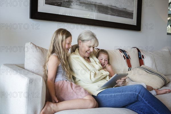 Caucasian grandmother and granddaughters using digital tablet on sofa