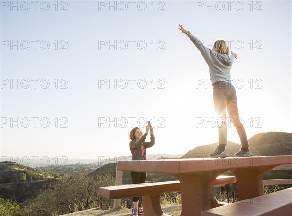 Caucasian woman photographing friend on hilltop