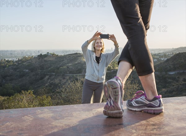 Caucasian woman photographing friend on hilltop