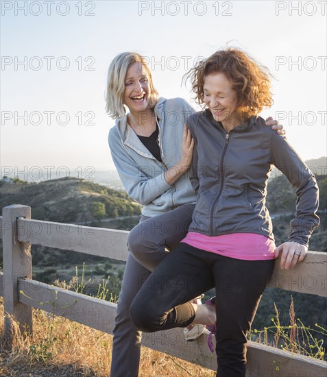 Caucasian women sitting on fence on hilltop