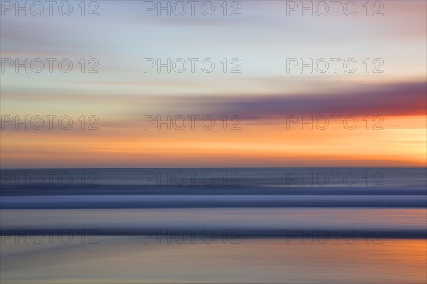 Defocused view of ocean waves on beach under sunset sky