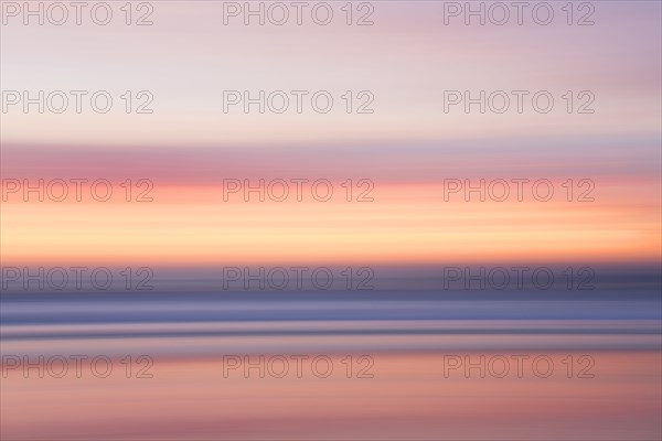 Defocused view of ocean waves on beach under sunset sky