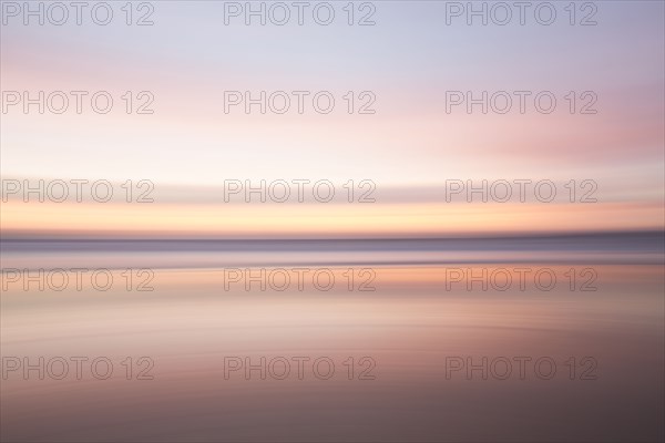 Defocused view of ocean waves on beach under sunset sky