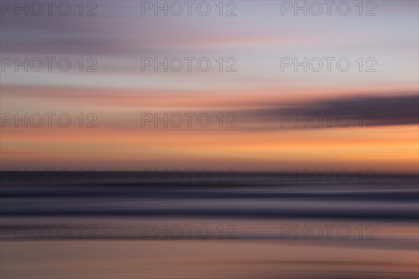 Defocused view of ocean waves on beach under sunset sky