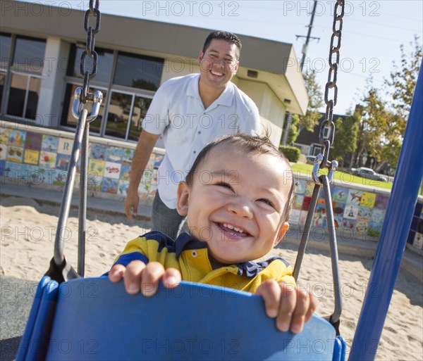 Hispanic father pushing son on playground swings