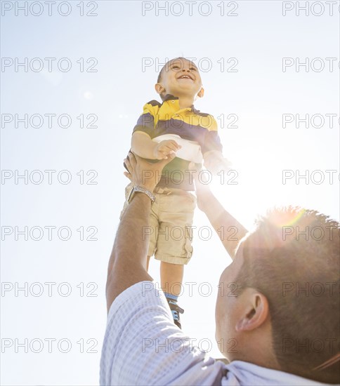 Low angle view of Hispanic father lifting son in air