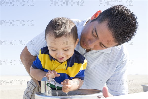 Hispanic father and son playing with water fountain