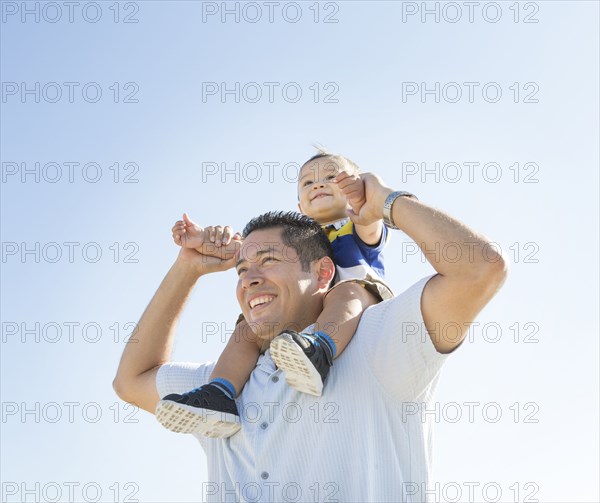 Low angle view of Hispanic father carrying son on shoulders