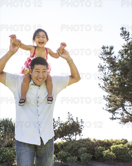 Hispanic father carrying daughter on shoulders