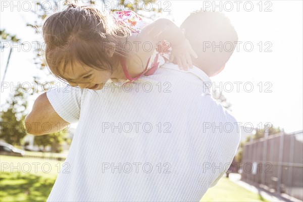 Hispanic father carrying daughter on shoulders