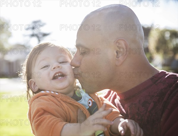 Close up of Hispanic father kissing cheek of son outdoors