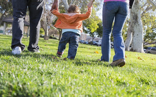 Hispanic mother and father helping son walk in park