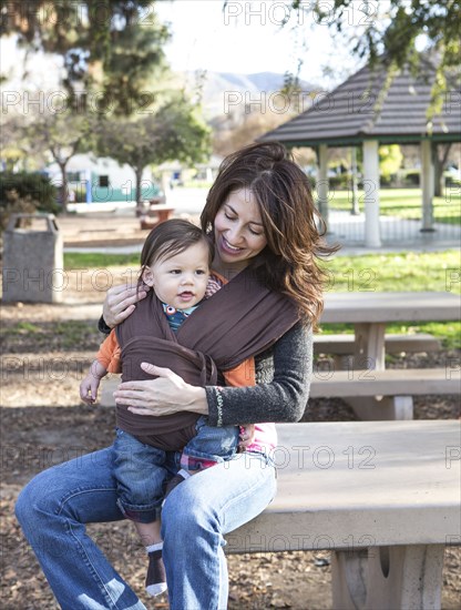 Hispanic mother wearing son in carrier in park