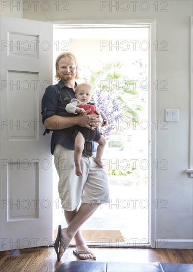 Caucasian father wearing son in harness in doorway