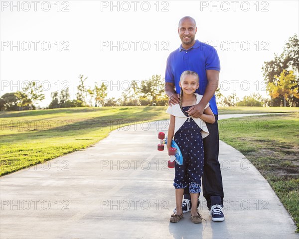 Father and daughter hugging with skateboard in park