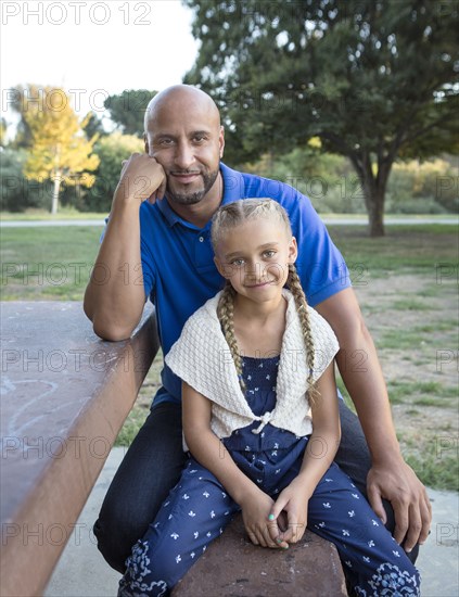 Father and daughter smiling on picnic table in park