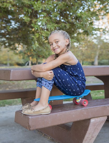 Mixed race girl sitting on skateboard on picnic table