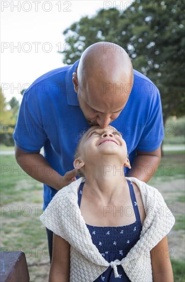 Father kissing forehead of daughter in park