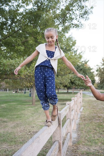 Father helping daughter balance on wooden fence