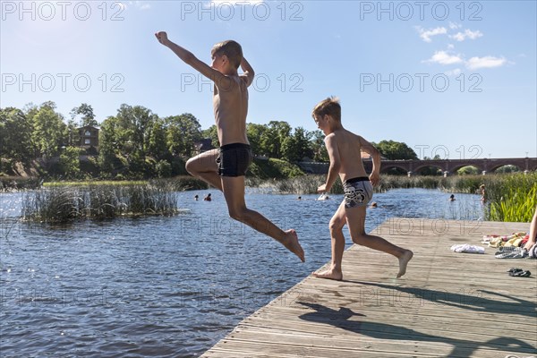 Caucasian children jumping into lake