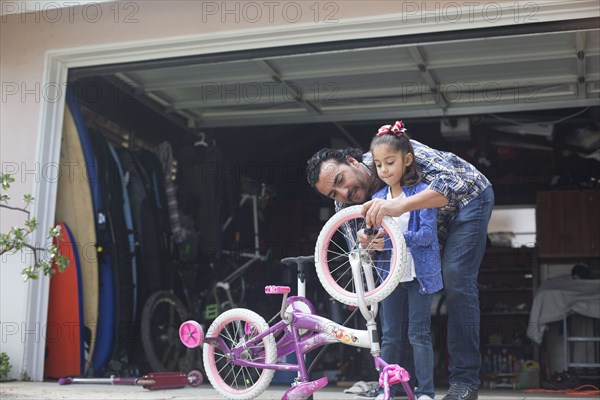 Hispanic father teaching daughter to repair bicycle