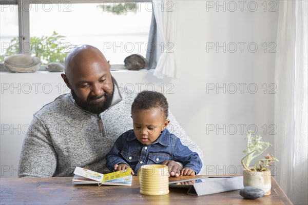 African American father and son reading book at table