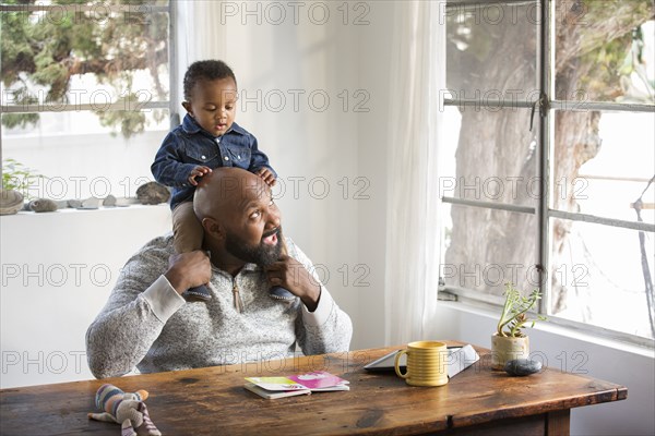 African American father holding baby son on shoulders