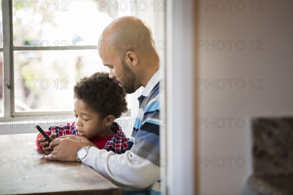 Mixed race father and son using cell phone at table