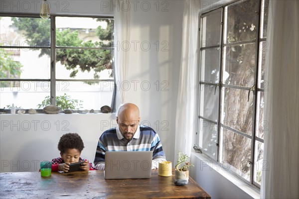 Mixed race father and son using technology at table