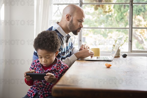 Mixed race father and son using technology at table
