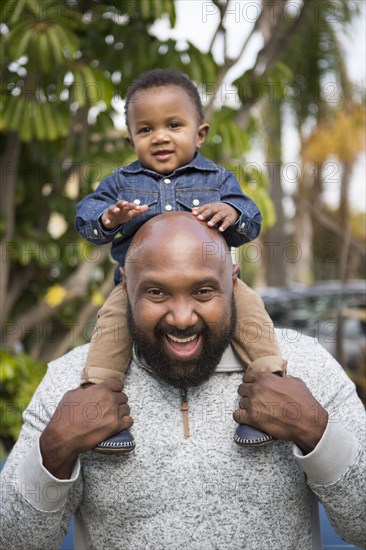 African American father carrying son on shoulders