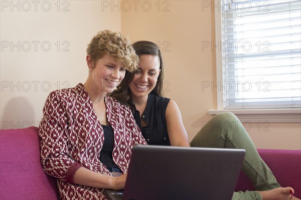 Caucasian lesbian couple using laptop on sofa