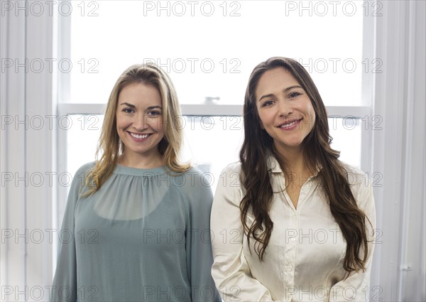 Caucasian businesswomen smiling near window