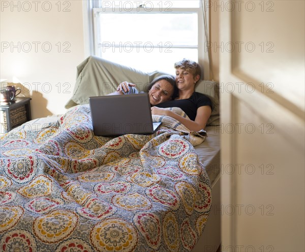 Caucasian lesbian couple watching laptop in bed