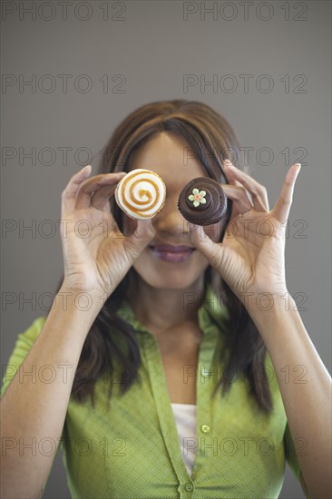 Mixed race woman holding cupcakes in front of her face