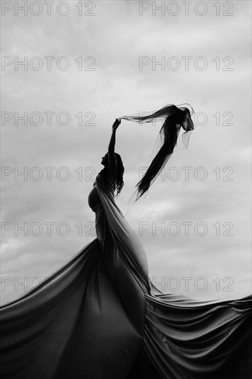 Caucasian woman twirling in fabric under clouds
