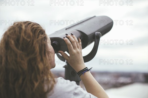 Caucasian woman on urban rooftop admiring cityscape with telescope